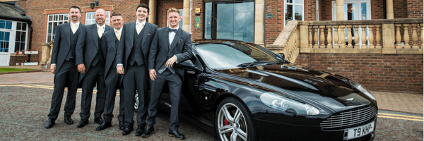 5 men in suits stood next to a black car 
